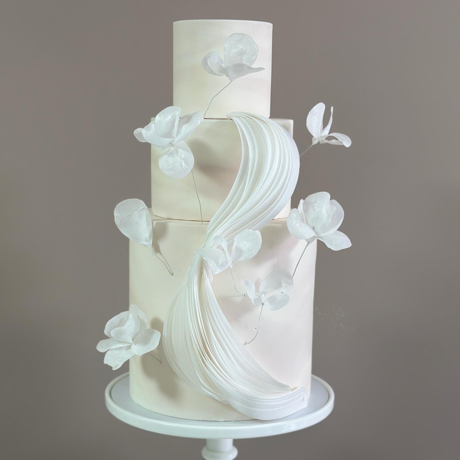 Ivory wedding cake with ruffled wafer paper swirl and magnolia flowers, luxury wedding cake London